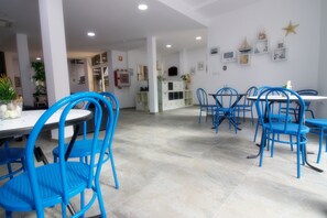 A spacious dining area with blue chairs and a white table, featuring a tiled floor and white walls with decorative items. - Hostal El Mercat (Villajoyosa)