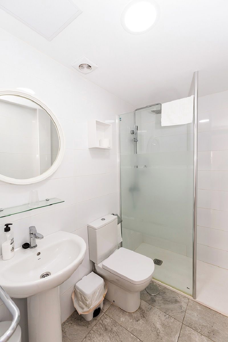 Une salle de bain moderne avec une douche à parois de verre, un miroir rond et un lavabo blanc.