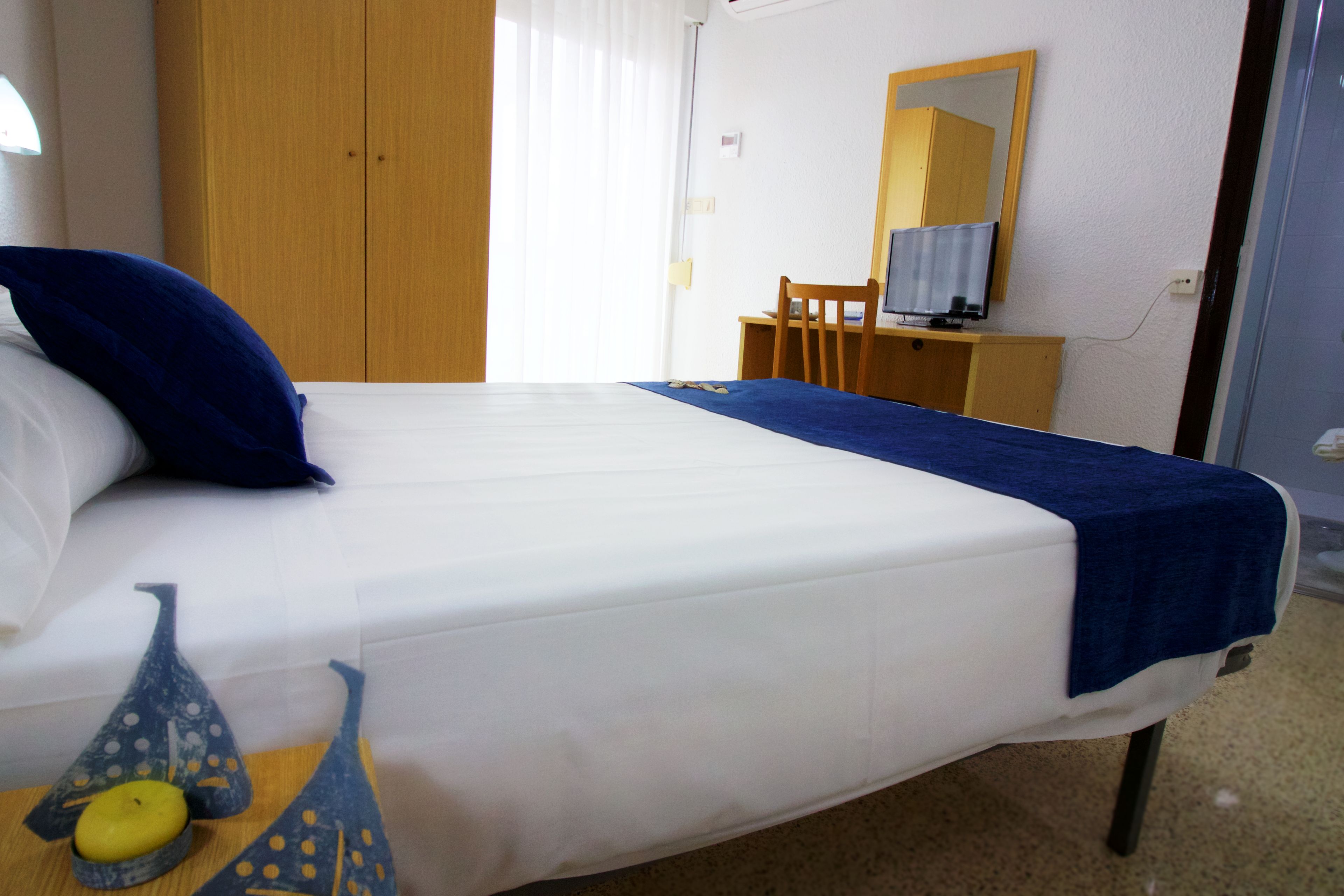 A hotel room with a bed, a desk, a chair, a mirror, and a window with curtains.