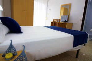 A hotel room with a bed, a desk, a chair, a mirror, and a window with curtains. - Hostal El Mercat (Villajoyosa)
