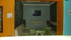 A room with a television mounted on the wall, a sofa, a small table, and a potted plant. - Hotel Naveen Residency (Darbhanga)