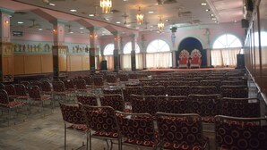 A conference room with rows of chairs, a stage with a backdrop, and ceiling fans. - Hotel Naveen Residency (Darbhanga)