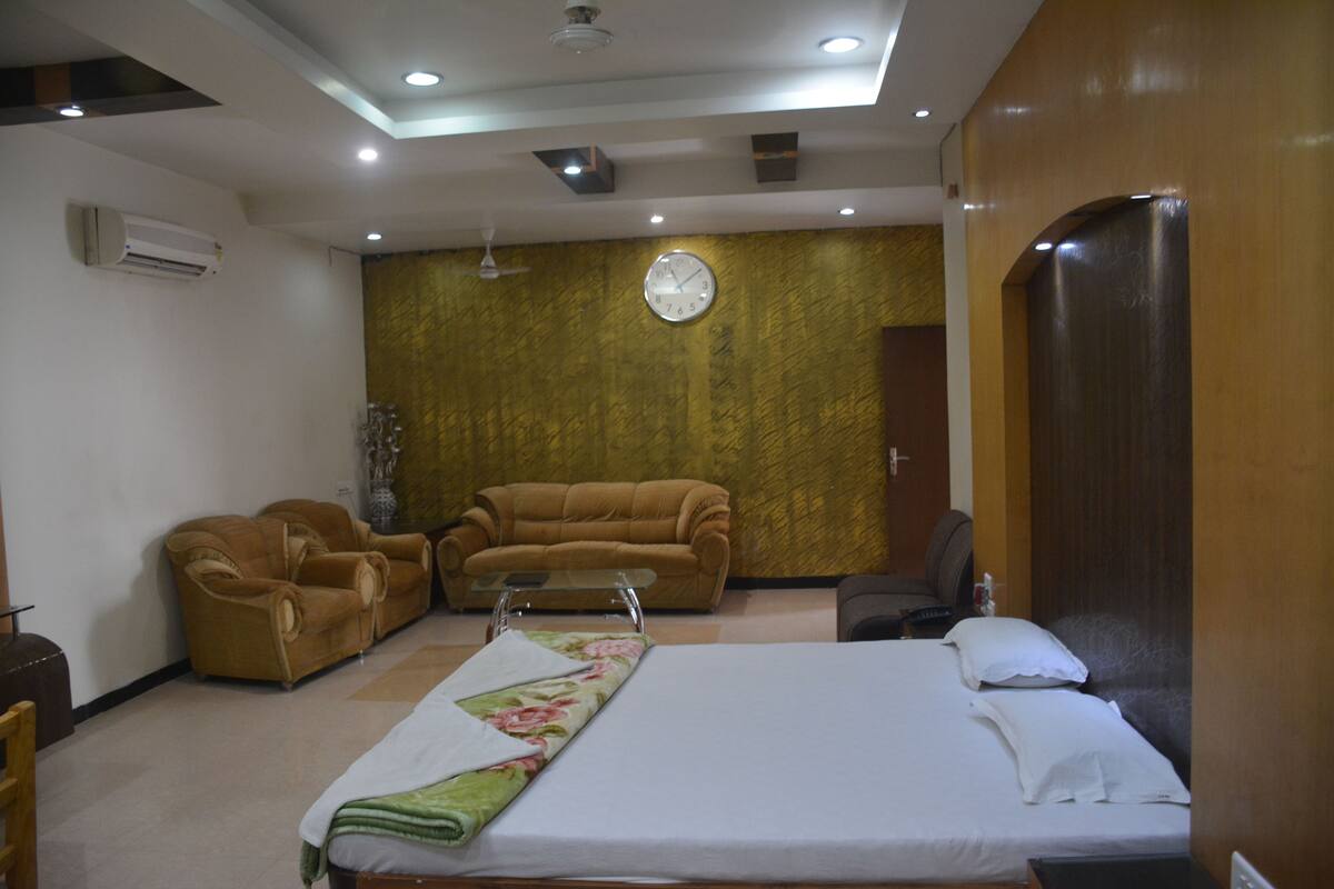 A hotel room with a bed, two sofas, a clock on the wall, and a wooden door.