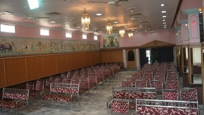 A large hall with rows of red and white patterned chairs, wooden paneling, and ceiling fans. - Hotel Naveen Residency (Darbhanga)