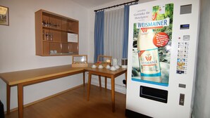 A hotel room with a wooden table, a small cabinet with glassware, a poster advertising Weismainer mineral water, and a window with blue curtains. - Hotel Spitzenpfeil (Michelau)