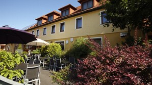 A yellow building with multiple windows and a red-tiled roof, surrounded by greenery and outdoor seating. - Hotel Spitzenpfeil (Michelau)