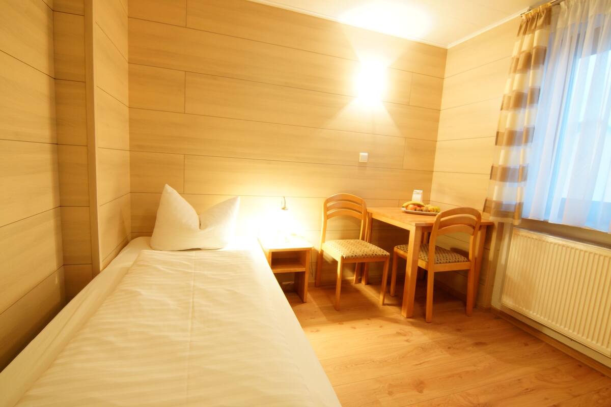 A hotel room with a bed, a small table with chairs, and a window with curtains.