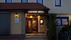 The exterior of the Gasthof Hotel with a sign above the entrance, a staircase leading to the door, and a small garden area with a chair and a table. - Hotel Spitzenpfeil (Michelau)