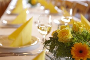 A table set with yellow napkins, a glass of white wine, and a floral centerpiece. - Hotel Spitzenpfeil (Michelau)
