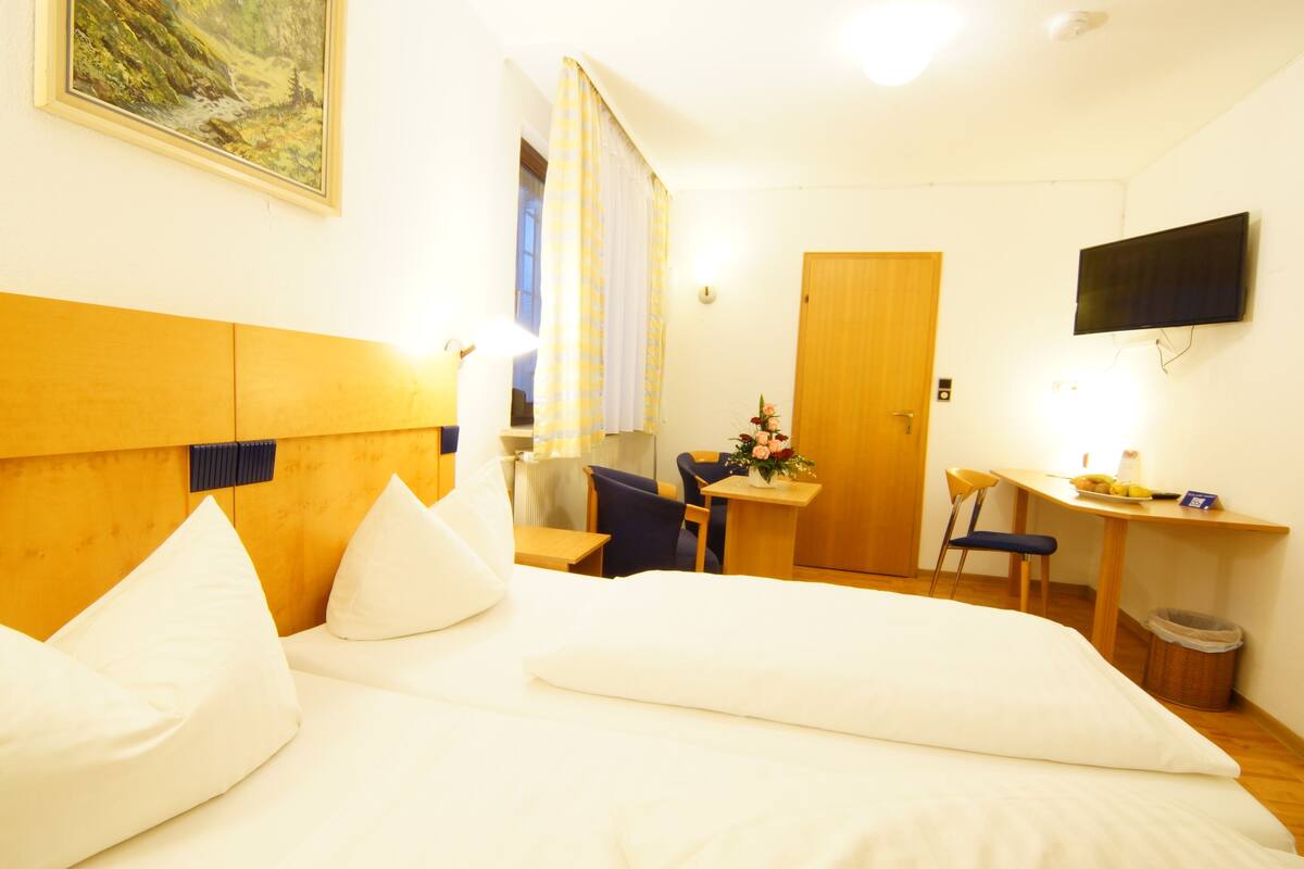 A hotel room with a bed, a desk, a chair, a TV, and a painting on the wall.