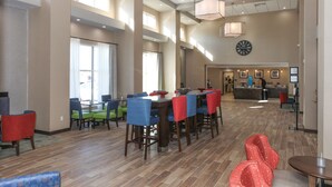 A spacious dining area with multiple tables and chairs, a kitchen in the background, and a clock on the wall. - Hampton Inn & Suites Lafayette Medical Center, CO (Lafayette)