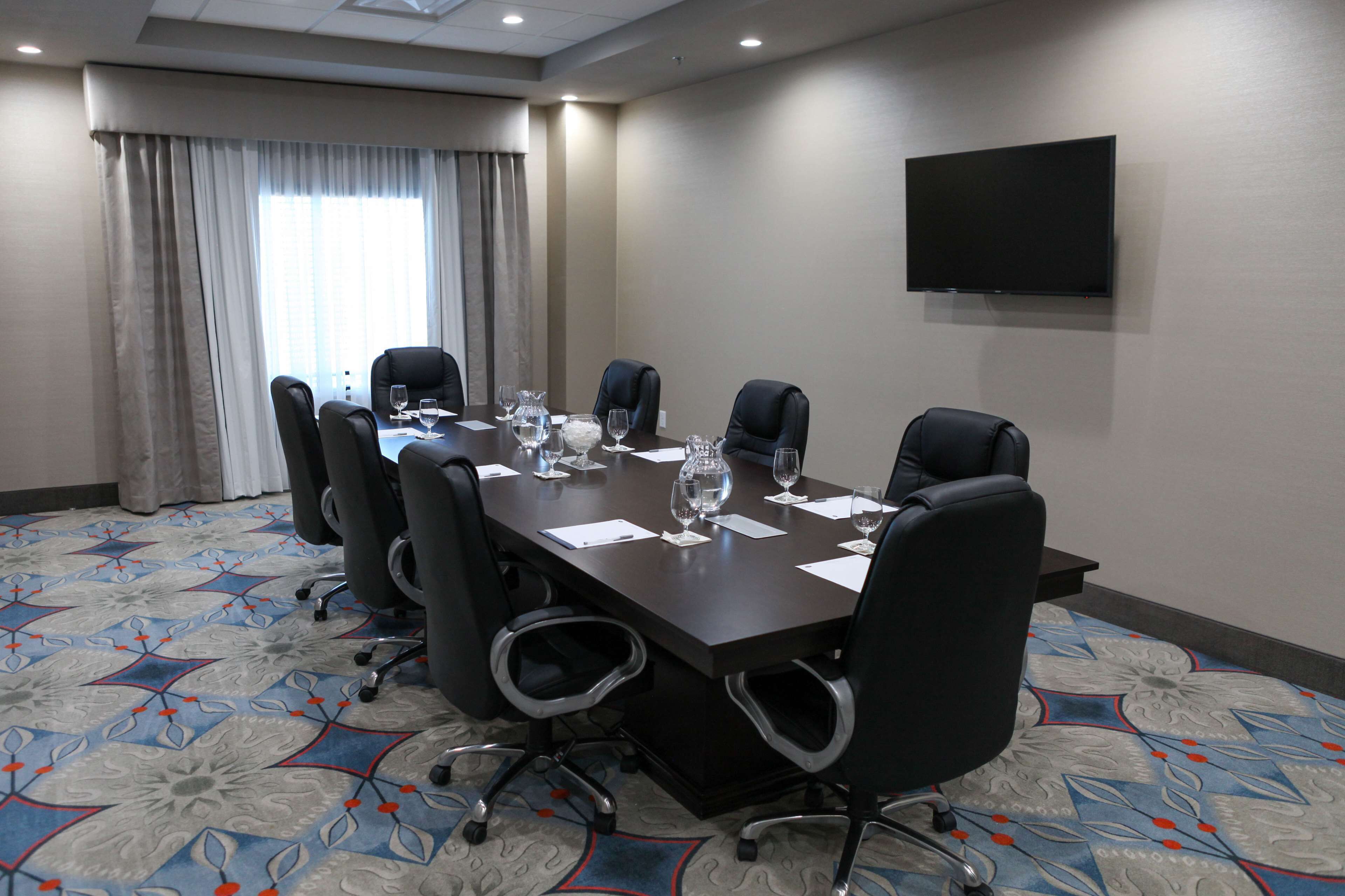 A conference room with a long table, six chairs, and a flat-screen TV on the wall.