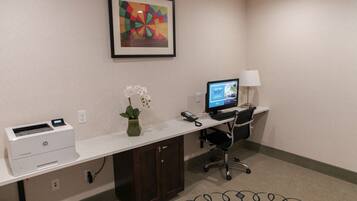 A hotel office with a desk, printer, computer, chair, lamp, and a framed artwork on the wall.