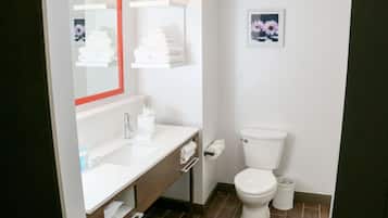 Une salle de bain moderne avec un lavabo blanc, un miroir et des toilettes. Des serviettes sont pliées et empilées sur une étagère au-dessus des toilettes.