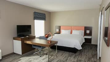 A hotel room with a bed, a desk with a TV, a lamp, and a window with a curtain.