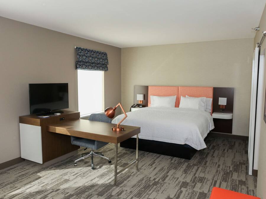 A hotel room with a bed, a desk with a TV, a lamp, and a window with a curtain.