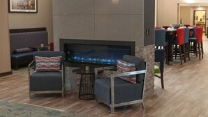 A modern lounge area with a stone fireplace, comfortable seating, and a dining area with red chairs. - Hampton Inn & Suites Lafayette Medical Center, CO (Lafayette)