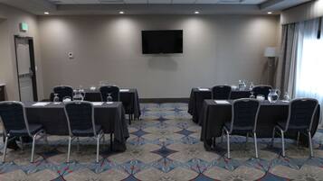 A conference room with tables, chairs, a flat-screen TV, and a patterned carpet.