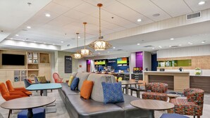 A modern hotel lobby with a seating area, a bar, and a coffee station. - Home2 Suites by Hilton McKinney (McKinney)