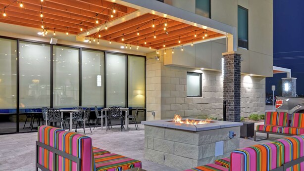 An outdoor patio with a fire pit, seating with colorful cushions, and string lights. - Home2 Suites by Hilton McKinney (McKinney)