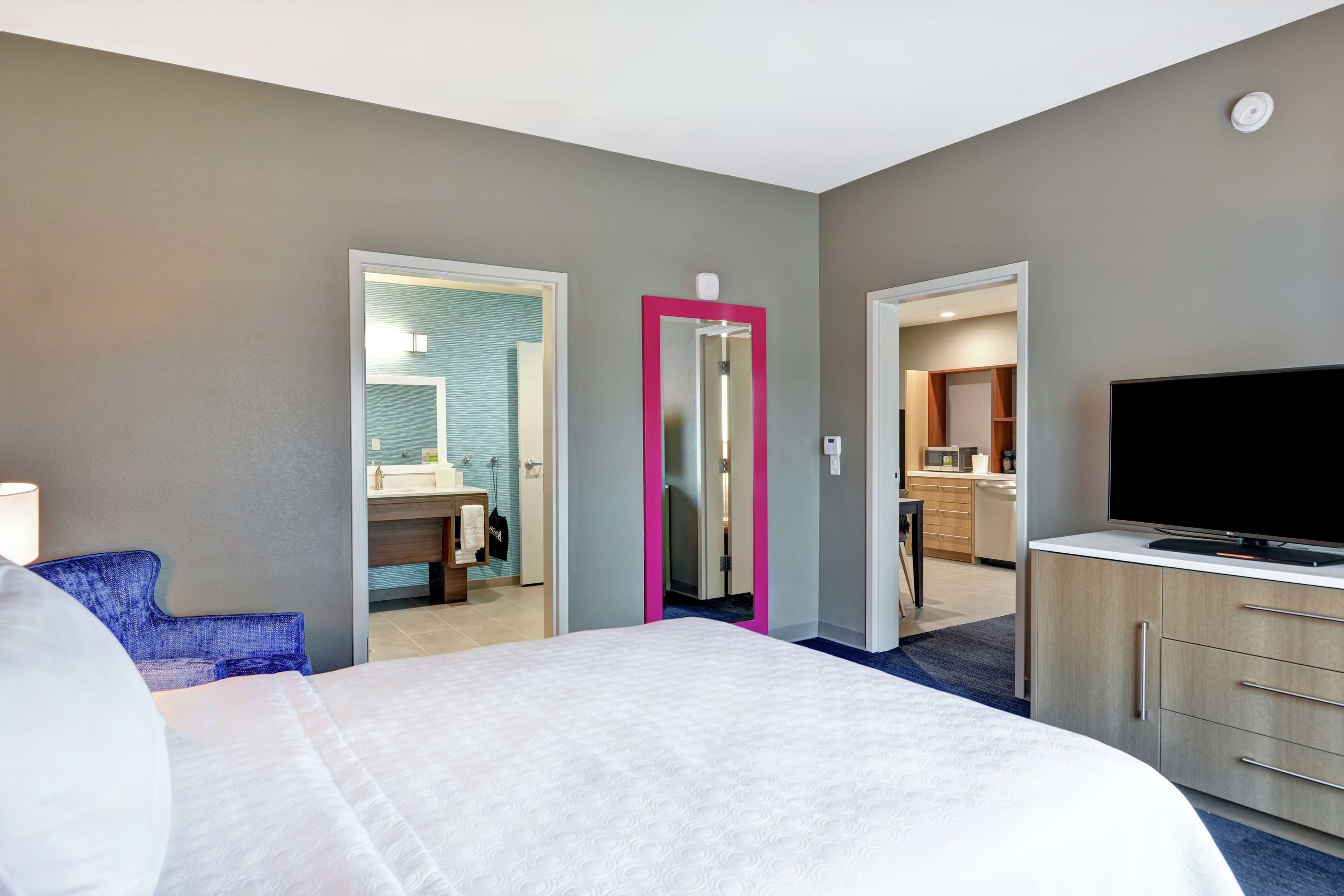 A hotel room with a bed, a TV, a desk, and a bathroom visible through an open door.
