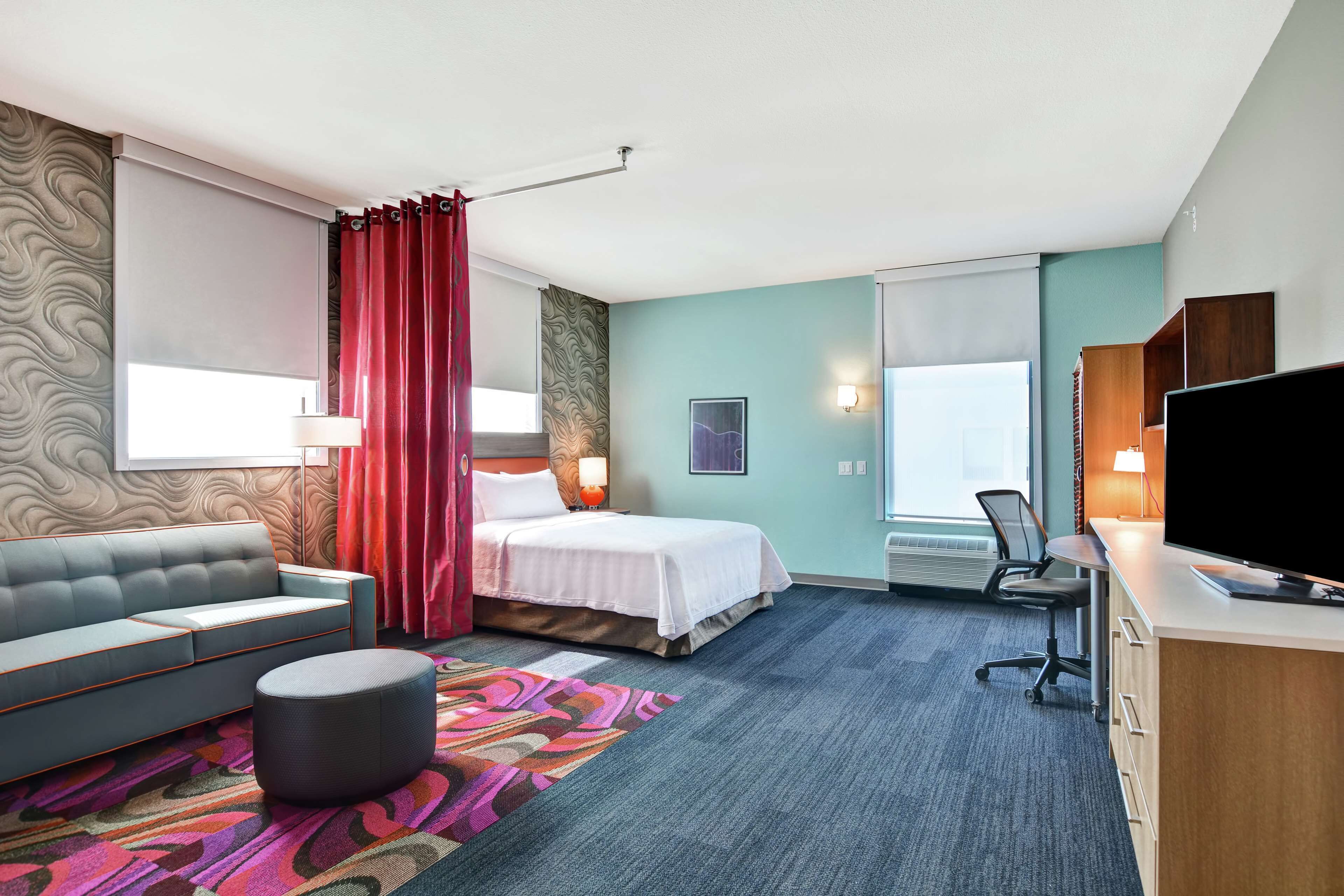 A hotel room with a sofa, a bed, a desk, a television, and a window with curtains.