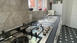 Een keuken met een gasfornuis, een magnetron en een spoelbak. Er is een raam met uitzicht op groen.