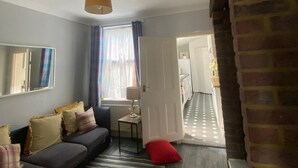 Een moderne woonkamer met een bank, een gestreept tapijt, een lamp en uitzicht op een hal die naar een keuken leidt.