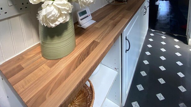 Een keuken met witte kastjes, een houten aanrechtblad, een vaas met witte bloemen en een digitale weegschaal.