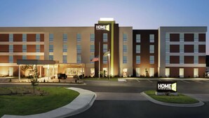 Un hotel de varios pisos con un llamativo letrero 'HOME 2', una bandera y una entrada bien iluminada.