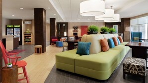 Un hall de hotel con un sofá verde, sillas rojas, un mostrador de recepción y un ventanal grande.
