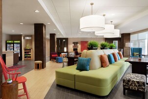 A hotel lobby with a green sofa, red chairs, a reception desk, and a large window.