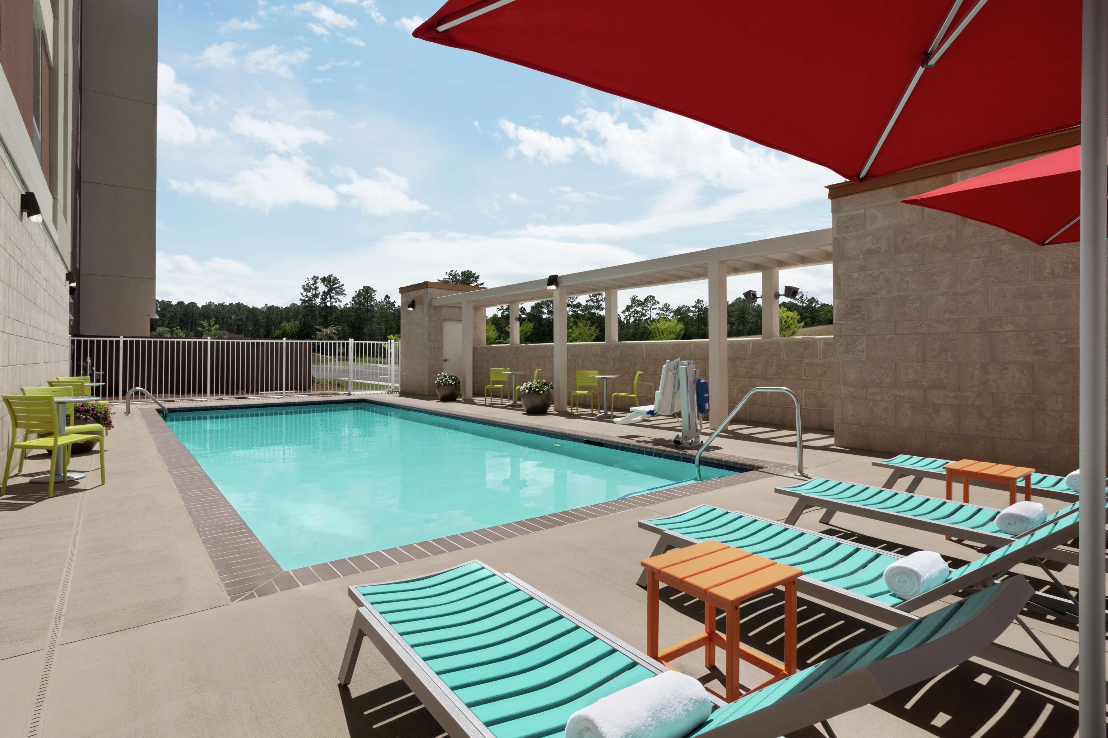 A swimming pool with lounge chairs and umbrellas, surrounded by a stone wall and a fence.