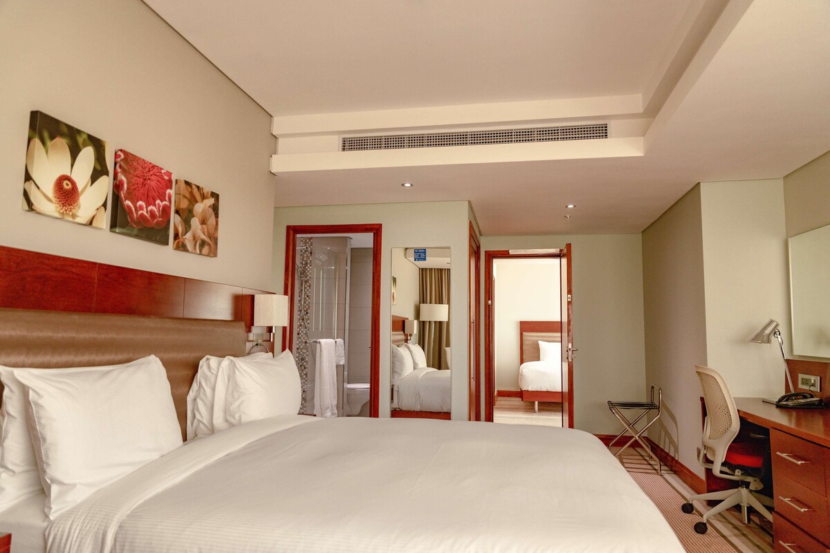 Una habitación de hotel con una cama grande, un escritorio con silla, un espejo y obras de arte en la pared.