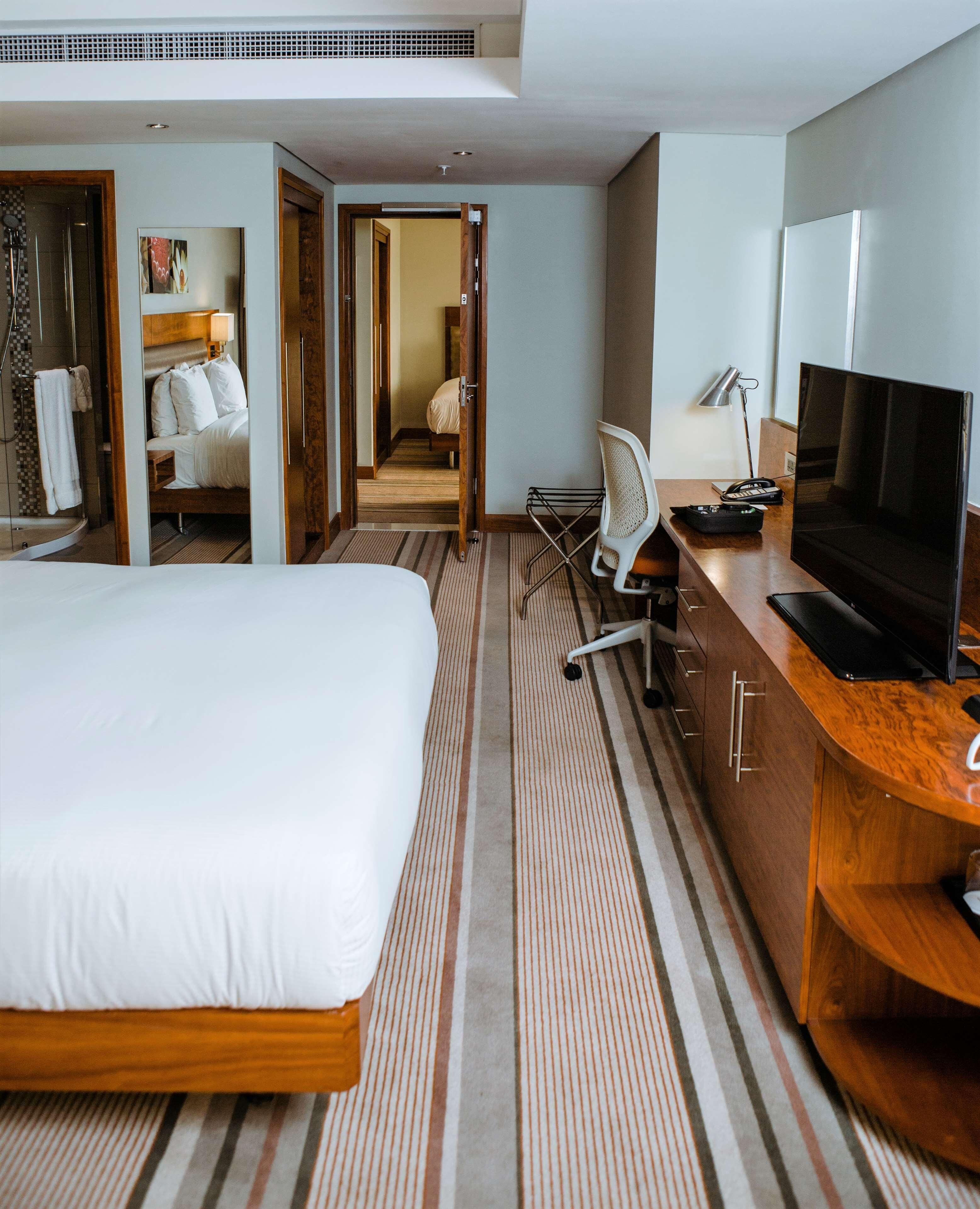 A hotel room with a large bed, a desk with a TV, a chair, and a shower area.