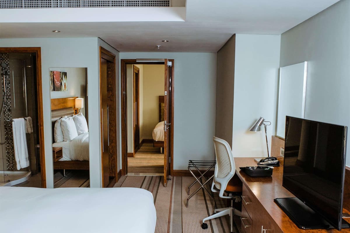 A hotel room with a large bed, a desk with a TV, a chair, and a shower area.
