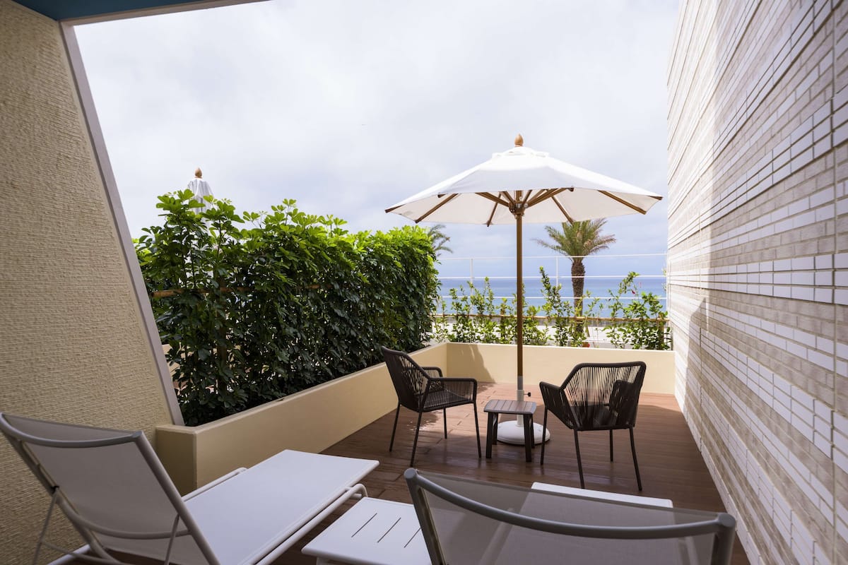 A balcony with a view of the sea, furnished with chairs and a table, and an umbrella.