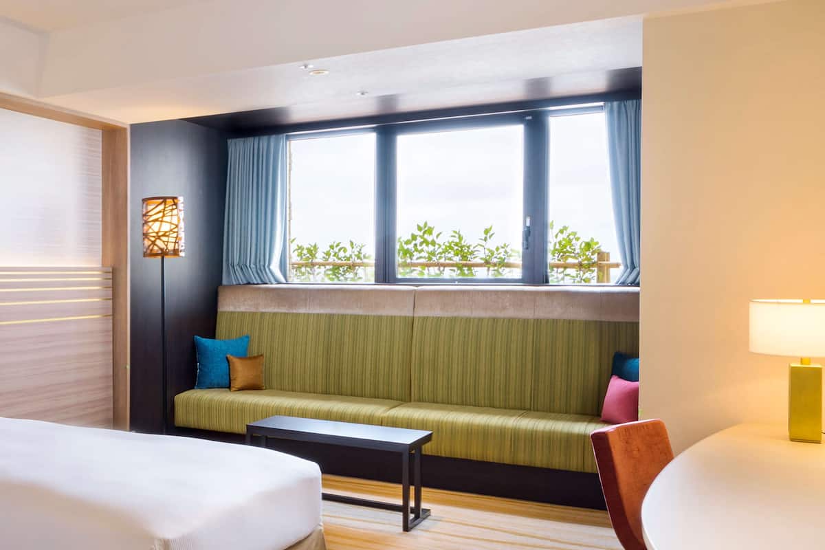 A hotel room with a green sofa, a small table, a bed, and a window with curtains.