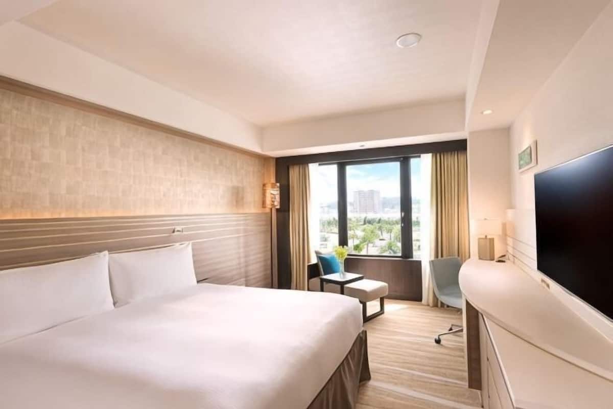 A hotel room with a large bed, a flat-screen TV, a small desk, and a window with a city view.