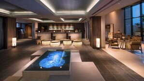 Un moderno vestíbulo de hotel con mostrador de recepción, zona de estar y piscina exterior climatizada.