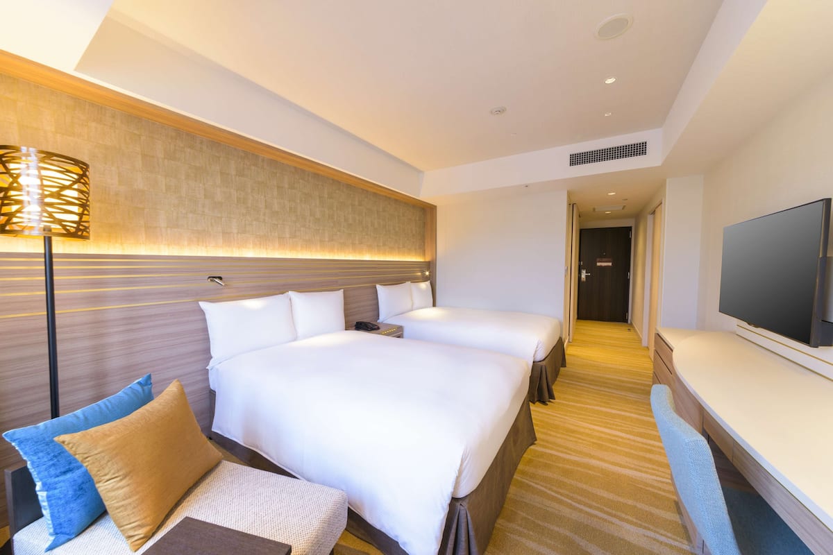 A hotel room with two beds, a sofa, a TV, and a lamp.