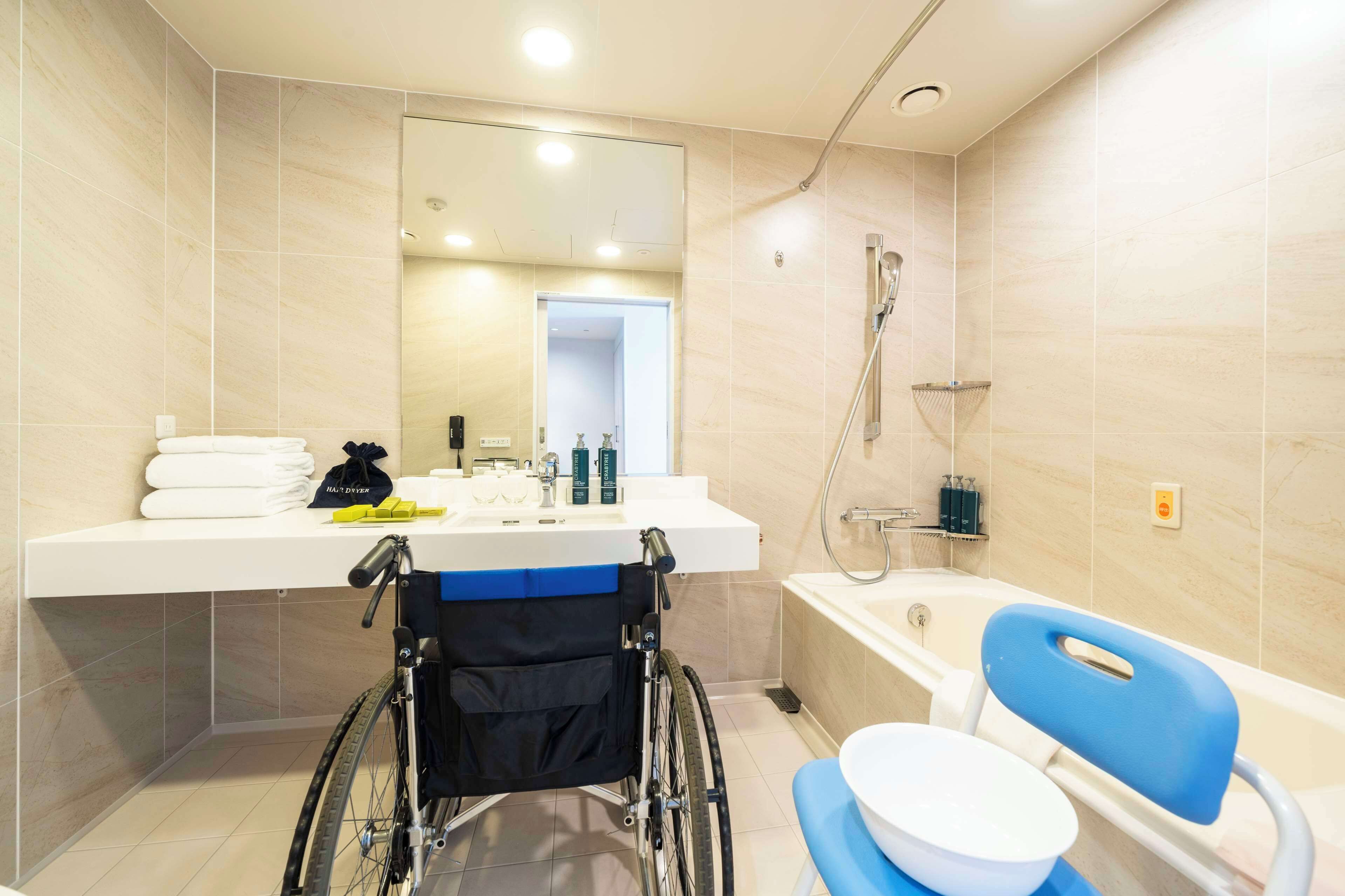 A modern bathroom with a wheelchair-accessible shower, a sink with toiletries, and a blue chair.