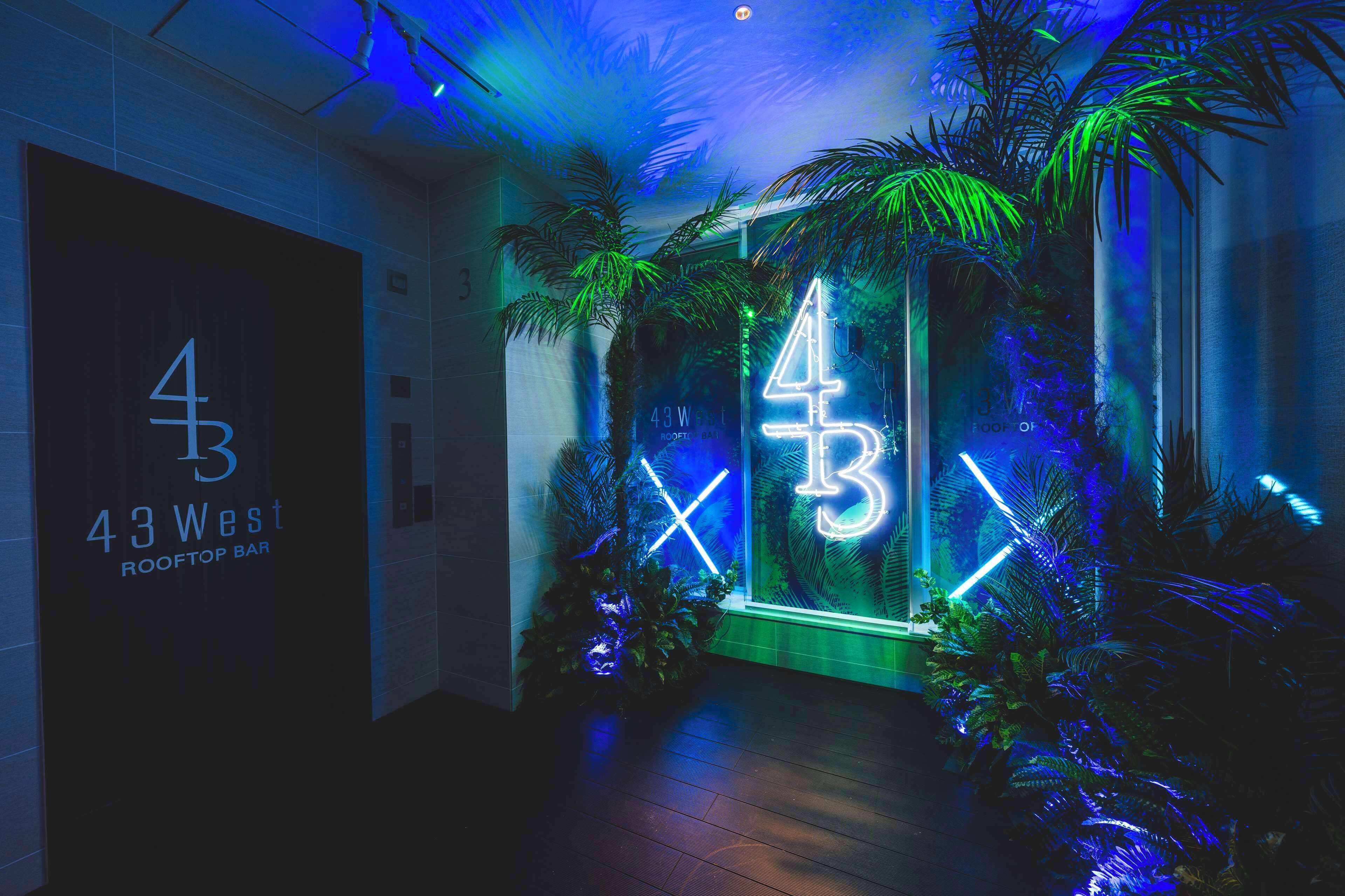 A hallway with a neon sign reading "43 West Rooftop Bar" and a large number "43" illuminated in neon lights.