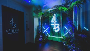 A hallway with a neon sign reading "43 West Rooftop Bar" and a large number "43" illuminated in neon lights.