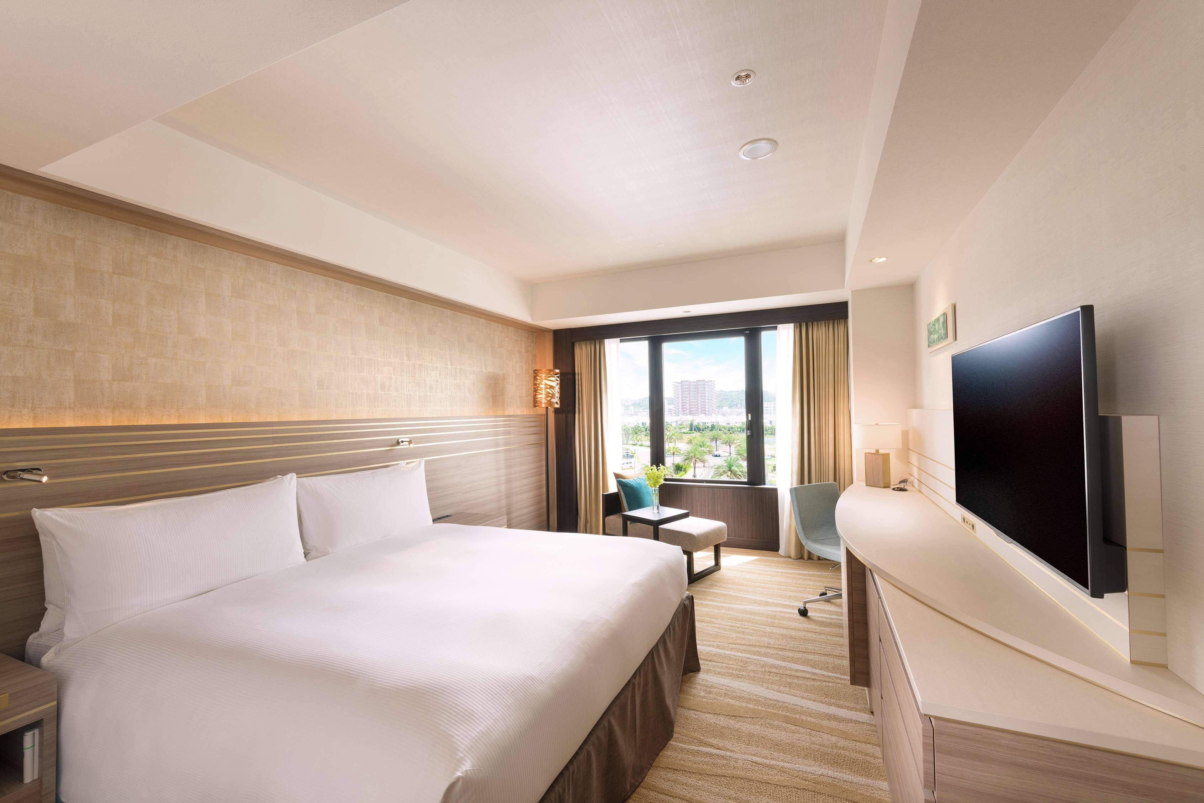 Une chambre d’hôtel avec un grand lit, un bureau, une chaise, une télévision et une fenêtre donnant sur la ville.