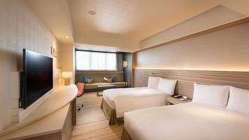 A hotel room with two beds, a flat-screen TV, a sofa, and a desk with a lamp.