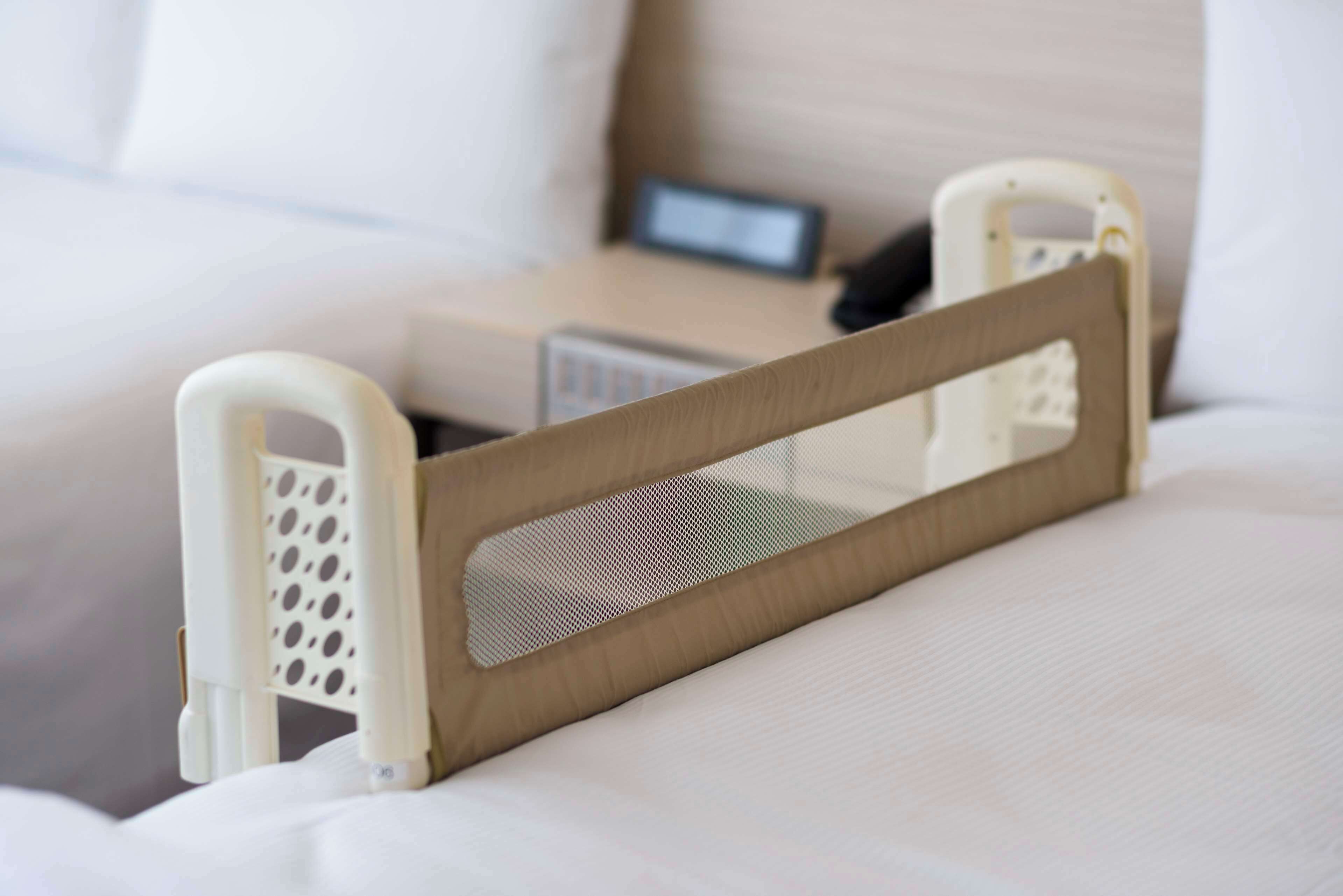 Una cama con colchón blanco, cabecera de madera y una barandilla de seguridad blanca.