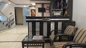 A reception area with a marble floor, a reception desk, a television, and striped chairs. - Hotel Apple Villa @ Paharganj (New Delhi)