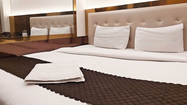 A neatly made bed with white linens, a brown quilted throw, and a folded white towel. - Hotel Apple Villa @ Paharganj (New Delhi)