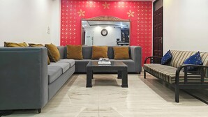 A living room with a grey sofa, a striped sofa, and a coffee table. - Hotel Apple Villa @ Paharganj (New Delhi)